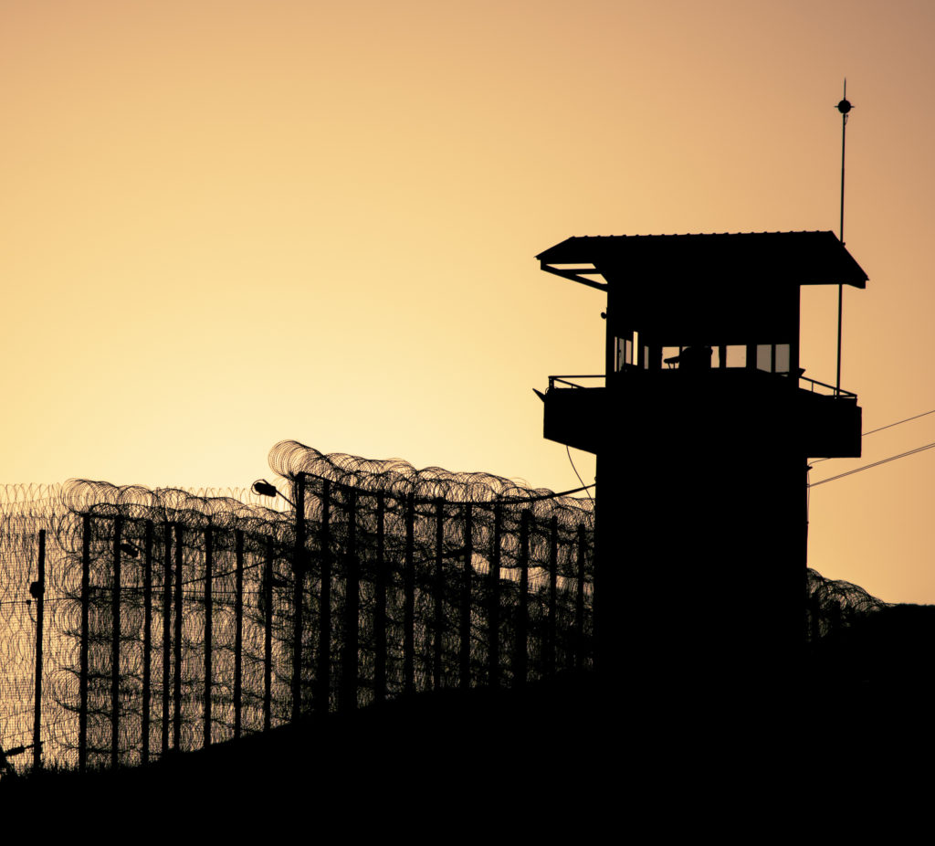 Silhouette of barbed wires and watchtower of prison, at sunset